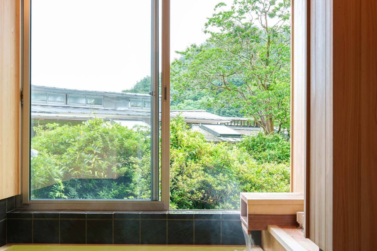 A wooden bathtub with a view of greenery and a building outside.