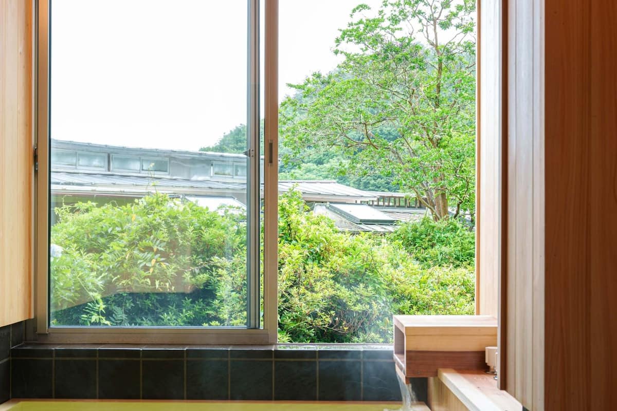 Una bañera de madera con vista a follaje y un edificio al exterior.