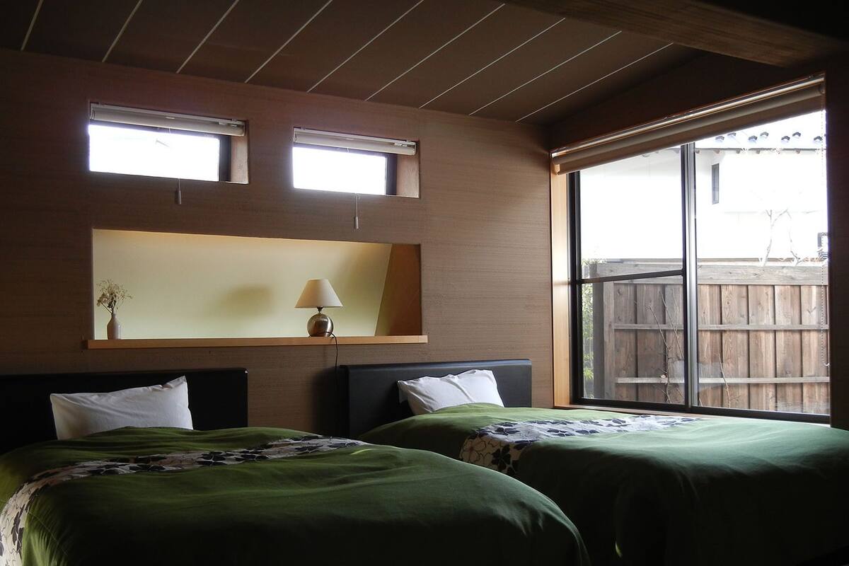 Un dormitorio con dos camas, una mesita de noche, una lámpara y una ventana que da a una cerca de madera.