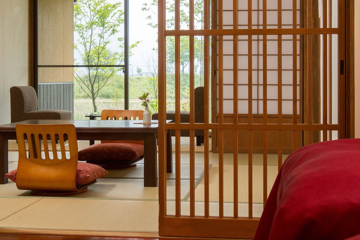 A traditional Japanese-style room with tatami flooring, a low wooden table, a cushioned chair, and a sliding shoji screen.