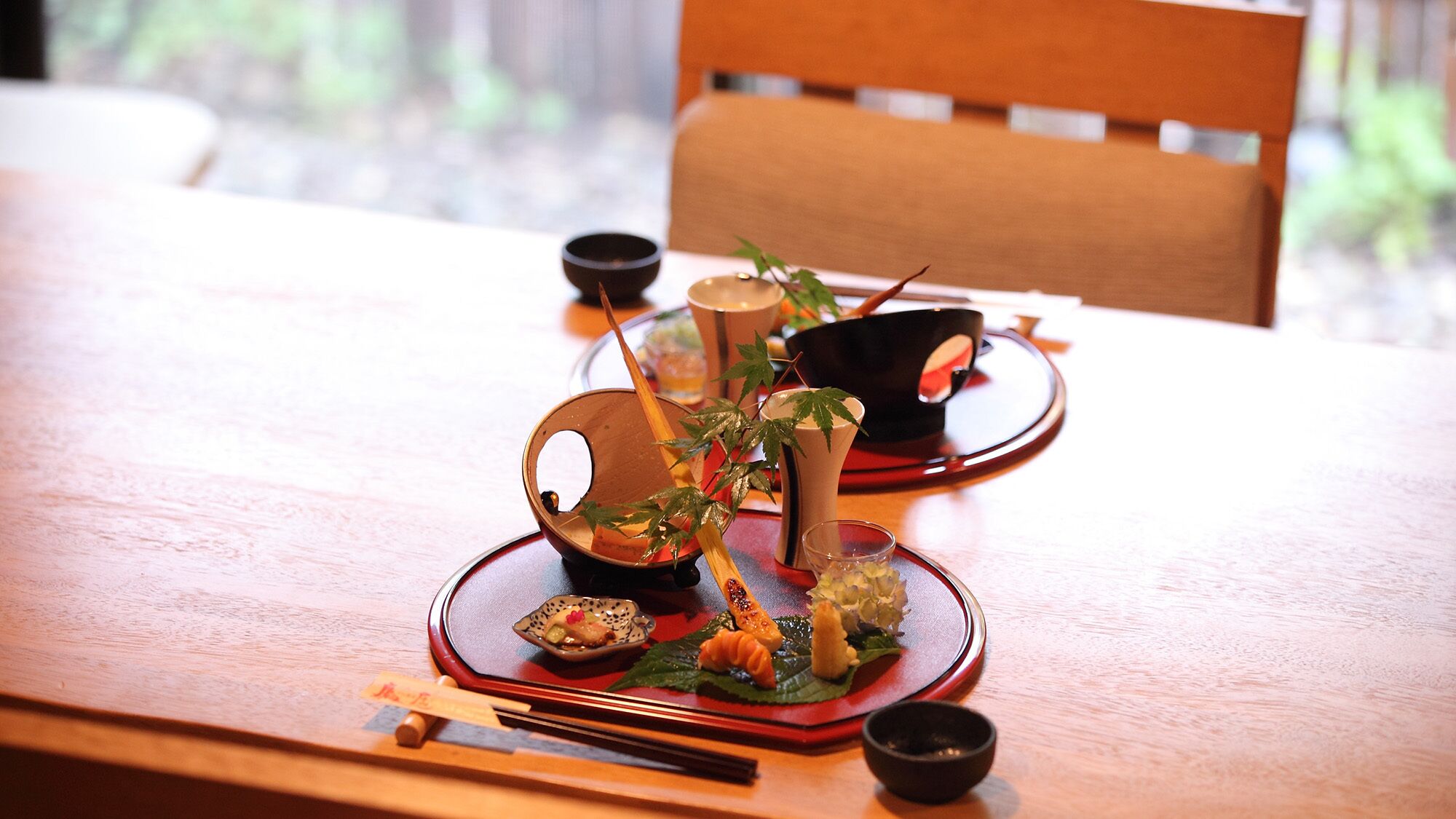 Una mesa de comedor con una disposición tradicional de comida japonesa, que incluye palillos, un tazón pequeño y un juego de té.