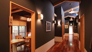 A hallway with wooden flooring, a dining area with a table and chairs, and wall-mounted lighting fixtures. - Takanosho (Aso)