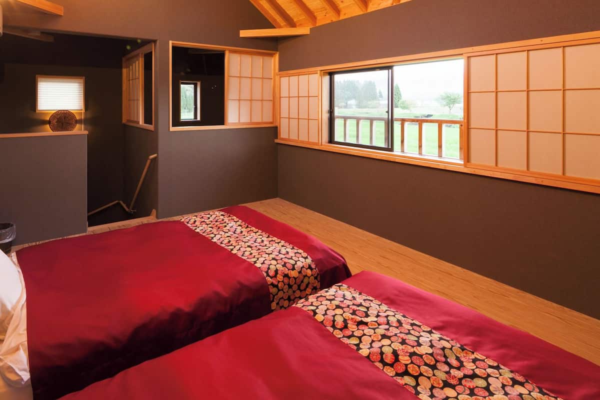 Una habitación con dos camas, un ventanal y un estante pequeño.