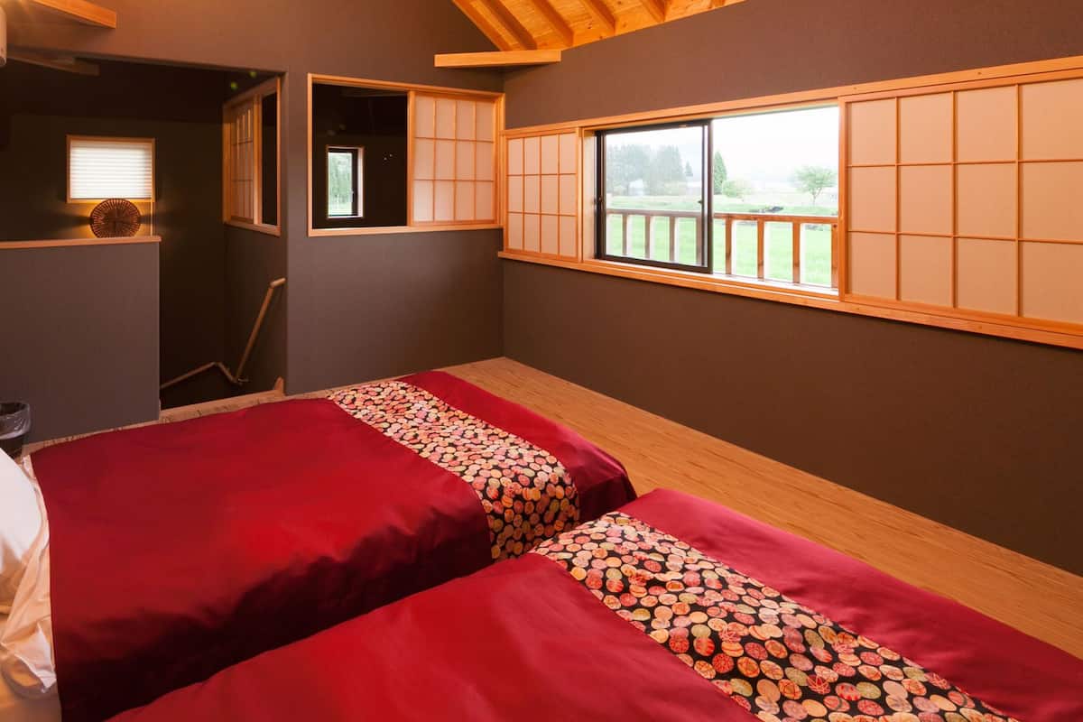 Una habitación con dos camas, una ventana con vistas, un estante pequeño y una puerta que da a otra estancia.