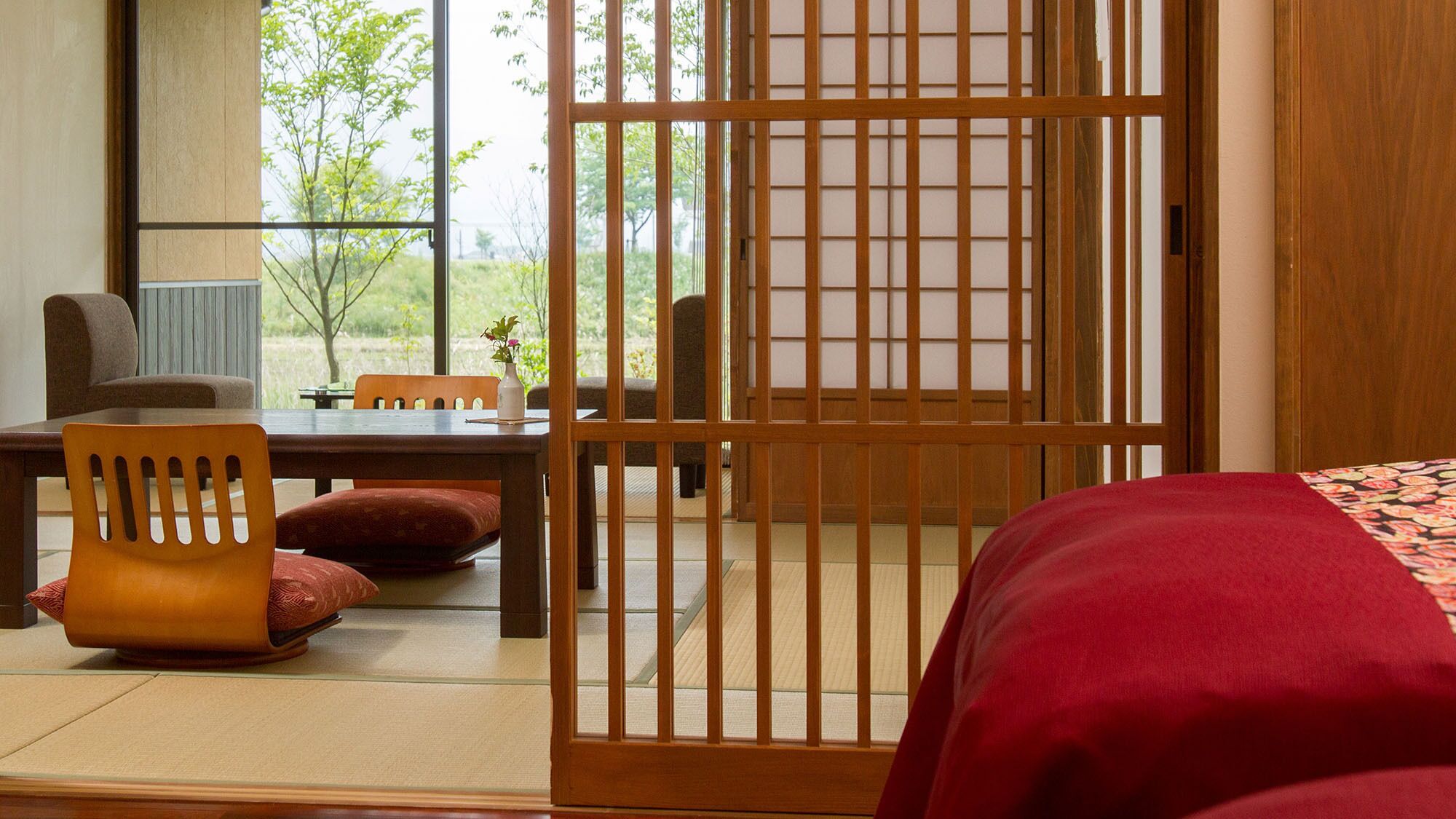 Una habitación japonesa tradicional con suelo de tatami, una mesa de madera baja, una silla acolchada y un panel corredizo shoji.