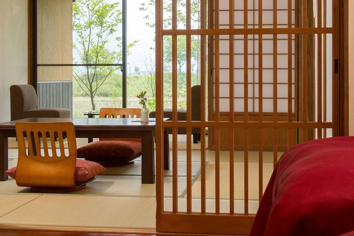 Una habitación japonesa tradicional con suelo de tatami, una mesa de madera baja, una silla acolchada y un panel corredizo shoji.