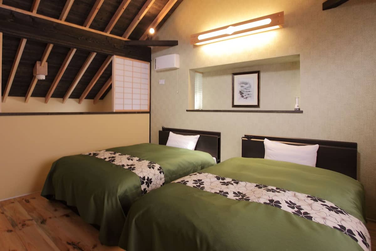 Una habitación con dos camas, vigas de madera en el techo, aire acondicionado de pared y un cuadro enmarcado.