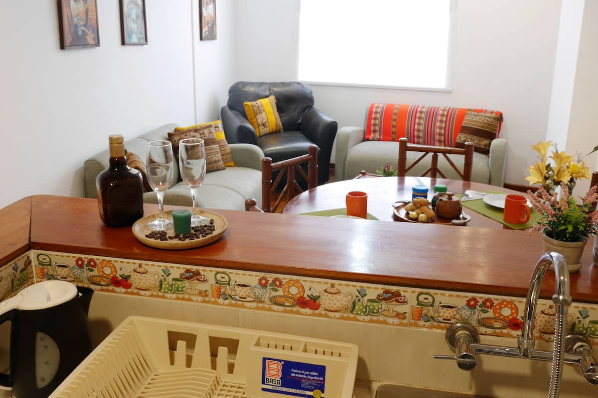 Uma sala de jantar com mesa de madeira, cadeiras, cafeteira e pia.