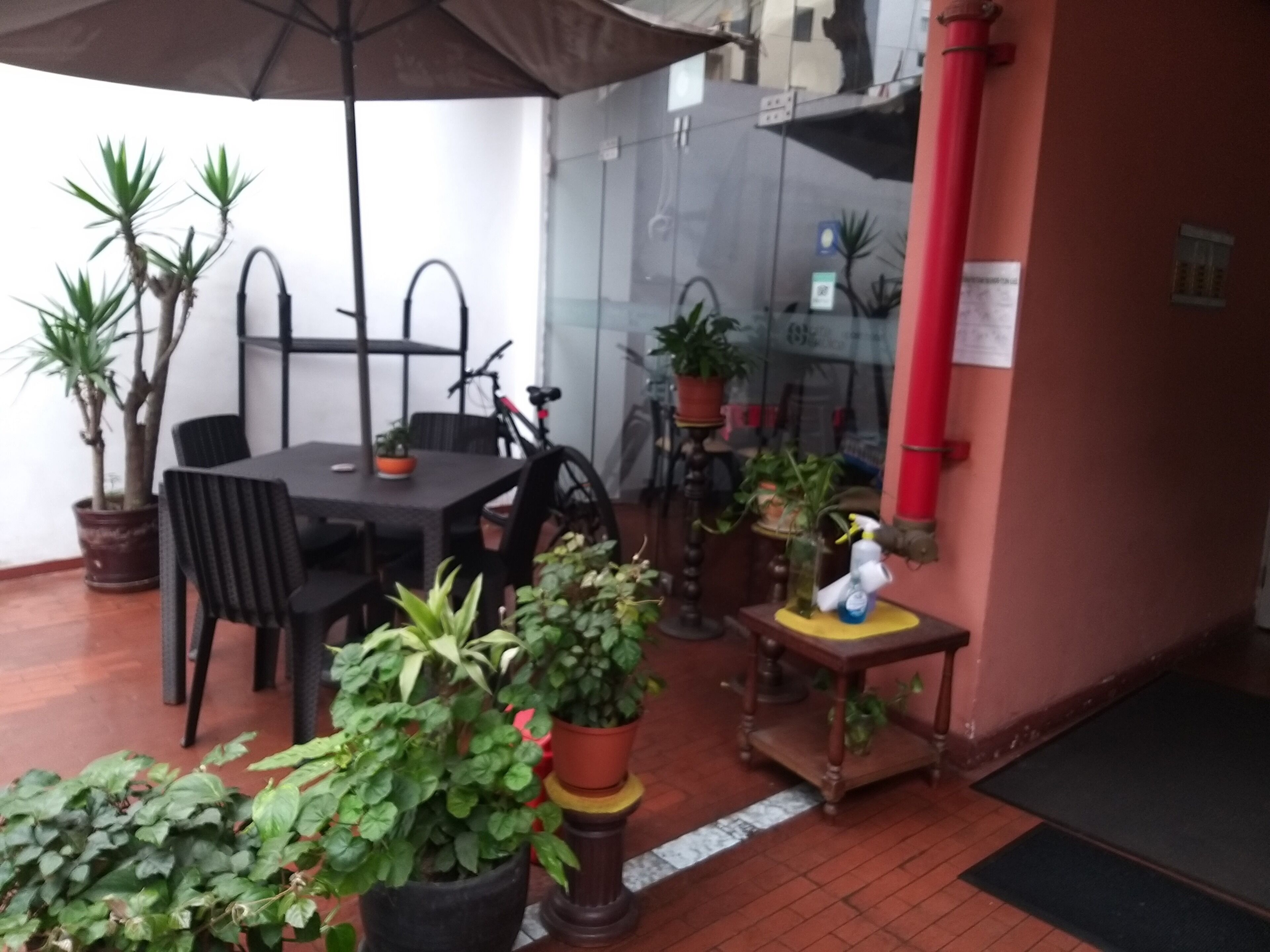 En udendørs terrasse med et bord og stole, plantekasser og en rød rør på væggen.