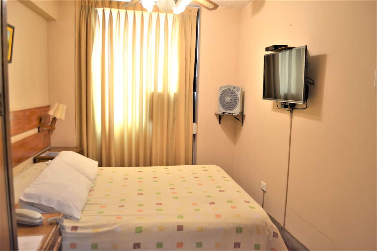 Quarto de hotel com cama, telefone ao lado, televisão na parede e janela com cortinas.