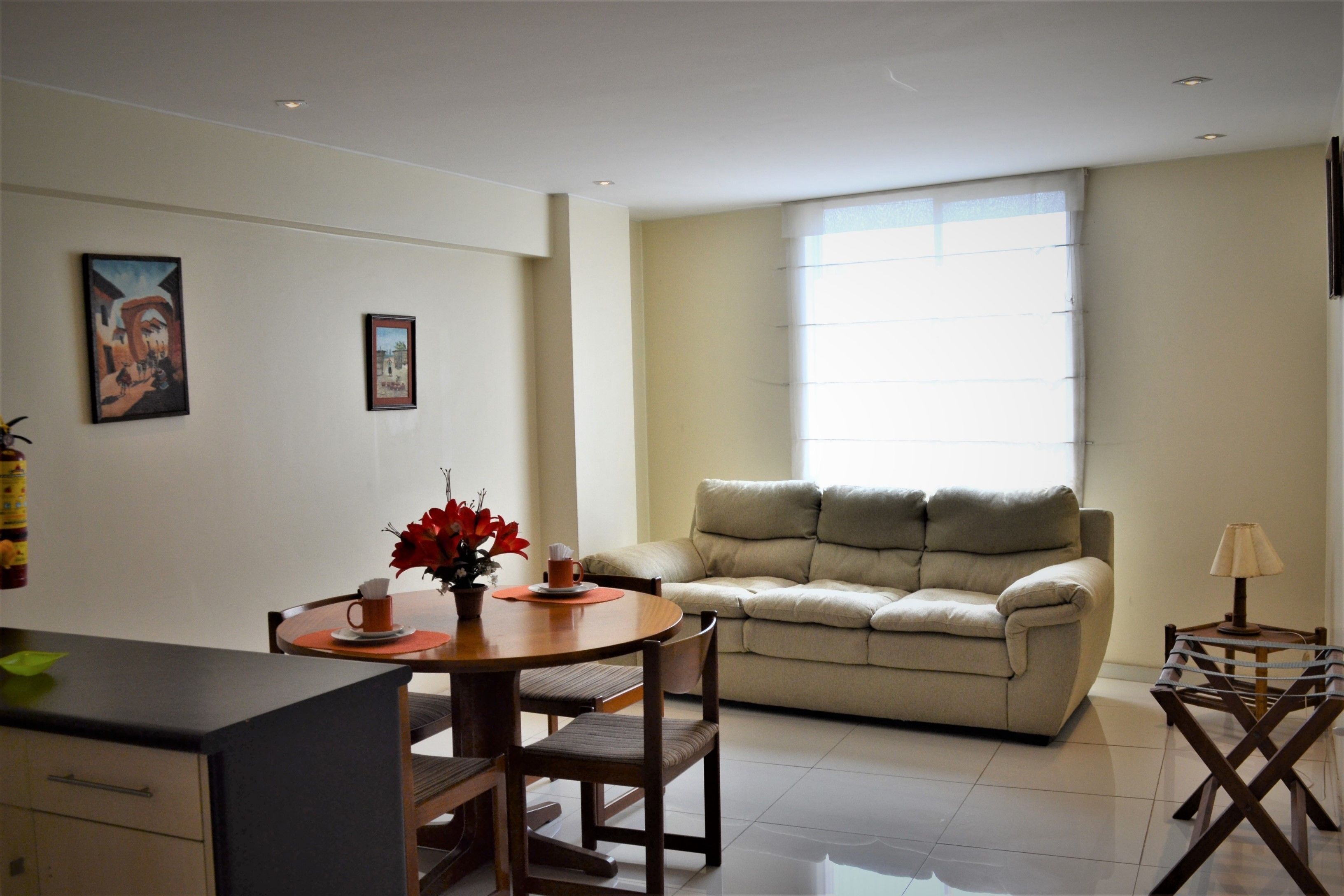 Ein modernes Wohnzimmer mit einer Couch, einem Esstisch mit Stühlen und einem Couchtisch. An der Wand hängen gerahmte Bilder und ein Fenster sorgt für natürliches Licht.