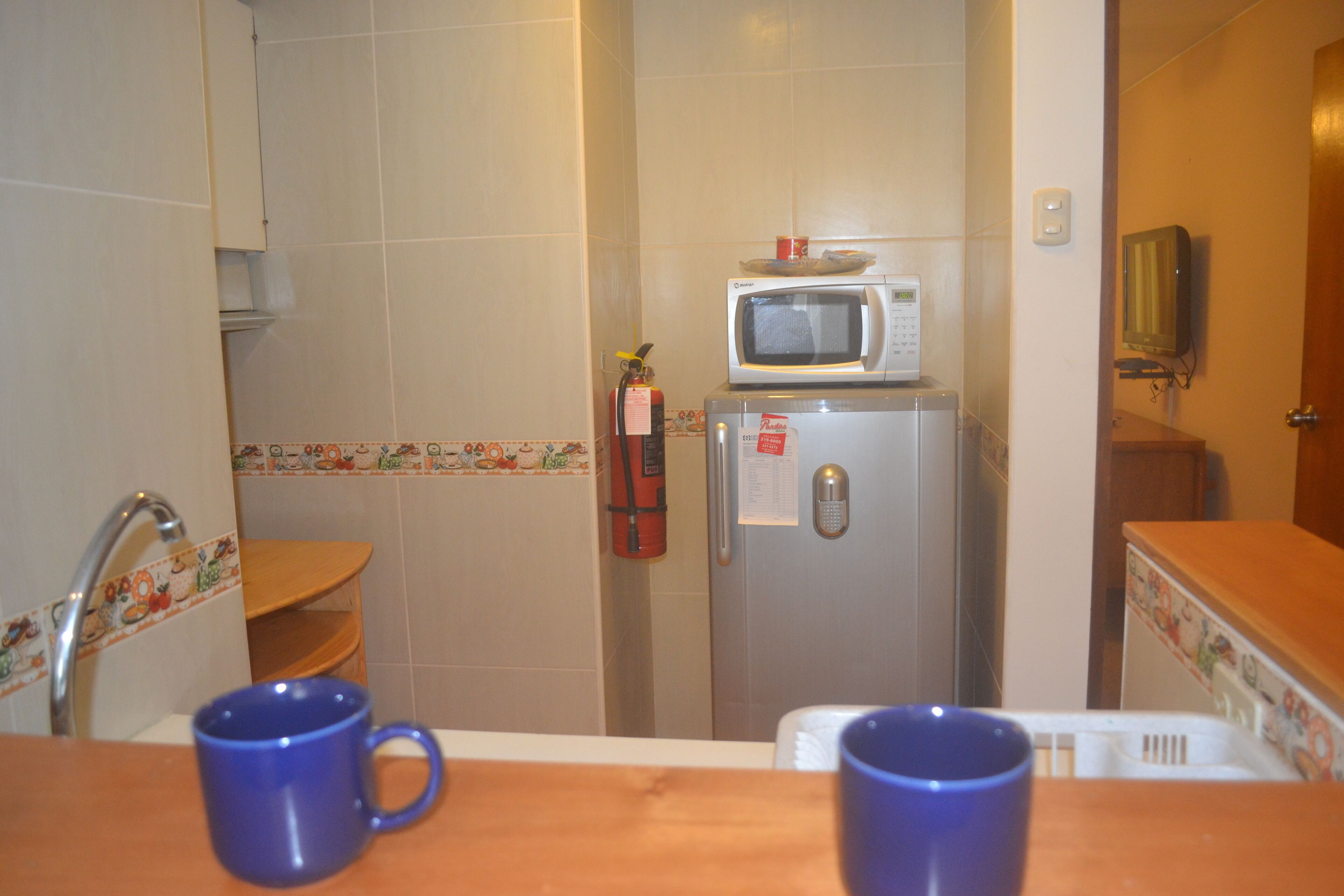 Pieni ja käytännöllinen keittiö, jossa on pieni jääkaappi, jonka päällä on mikroaaltouuni, sammutin ja pesuallas hanalla.