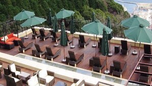 Un área de piscina en la azotea con sillones y sombrillas, con vistas a una ciudad costera.