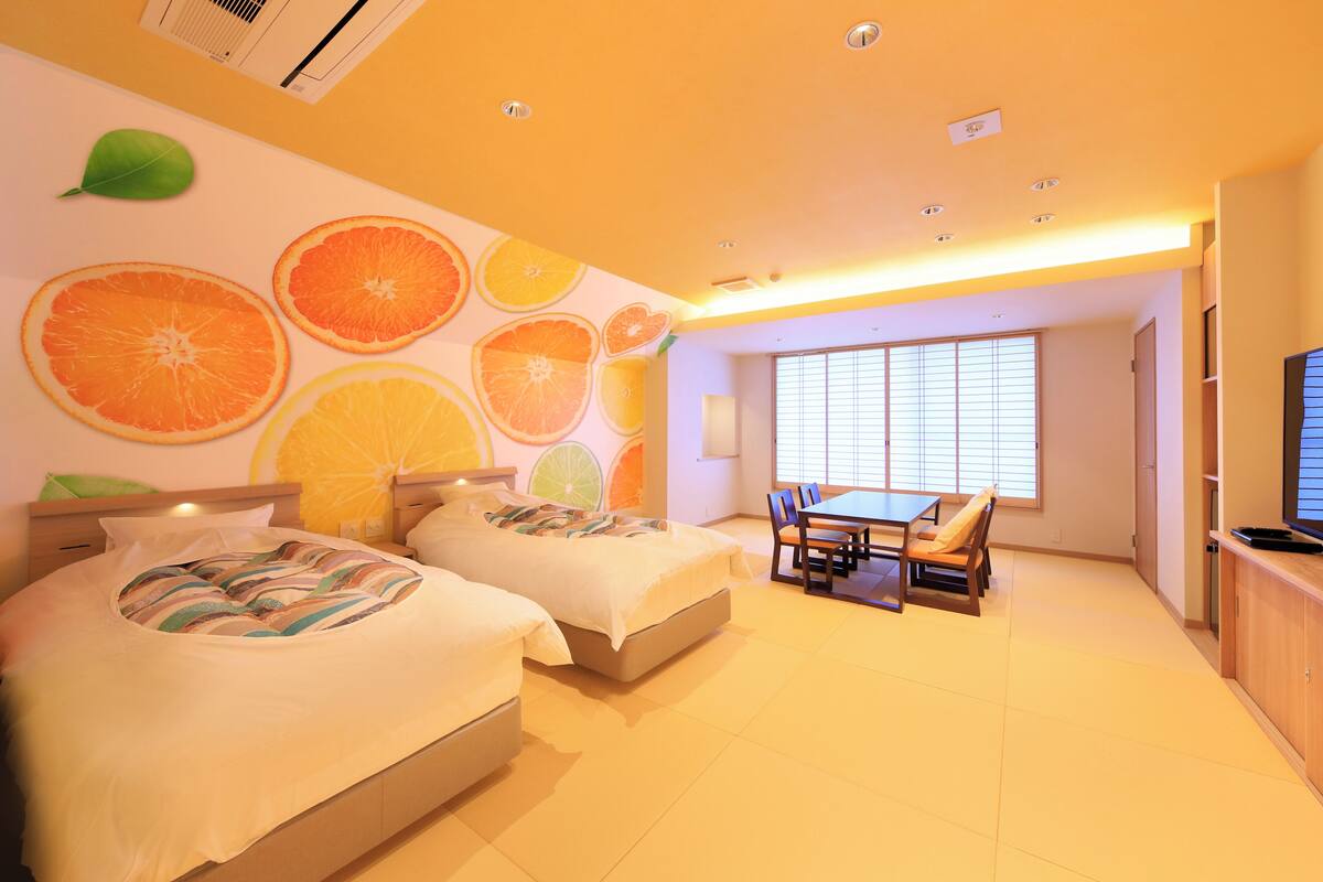 A hotel room with two beds, a dining area, and a large window.