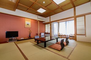 A traditional Japanese-style room with tatami flooring, a low table with cushions, a television, and a large window with curtains. - Yuyado Mikan No Ki (Atami)