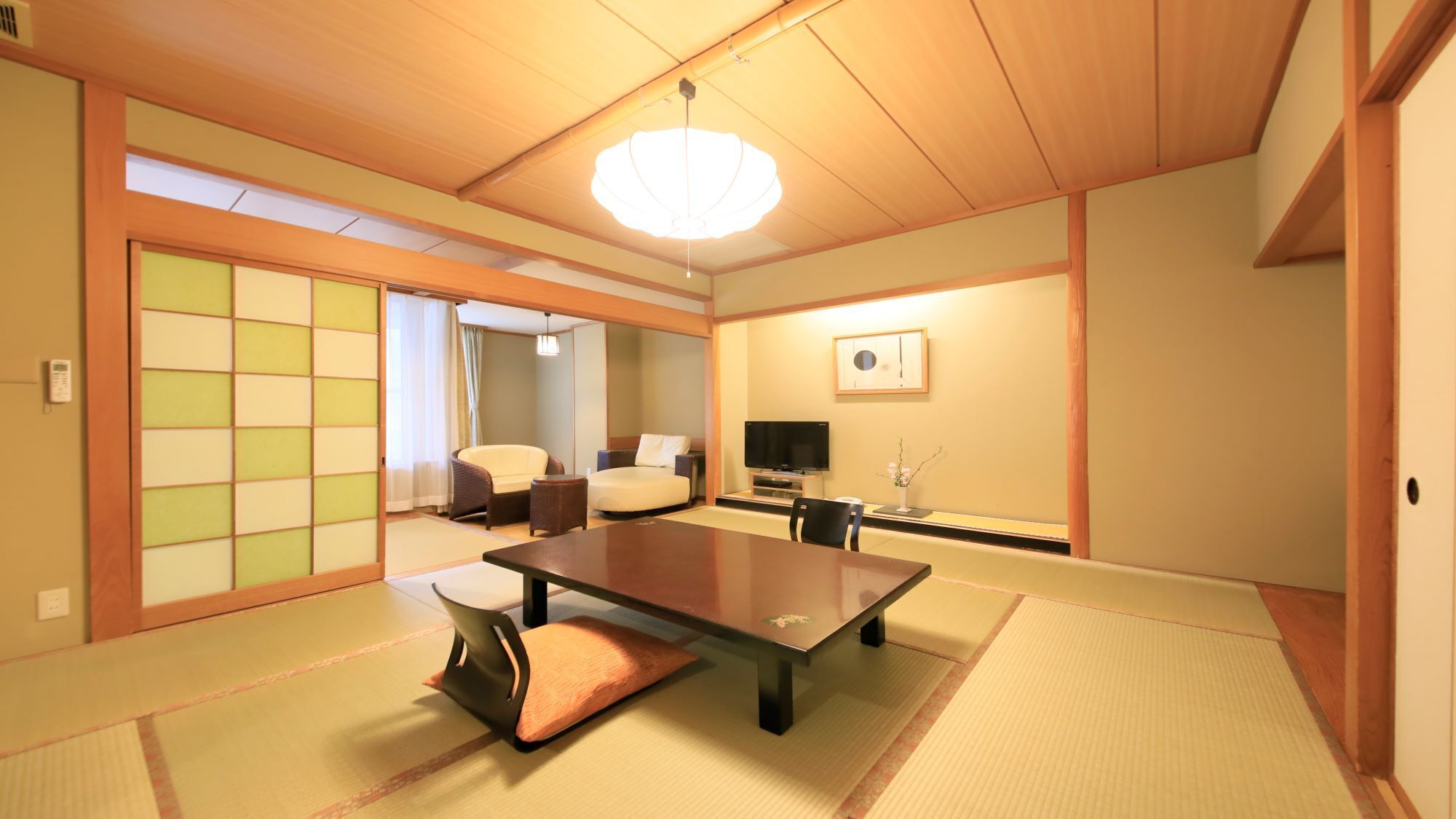 Una habitación japonesa tradicional con suelo de tatami, una mesa baja, sillas, un televisor y una puerta corrediza.