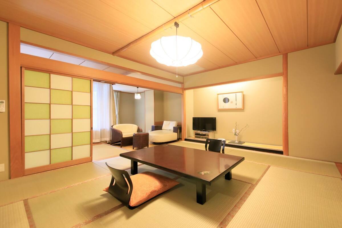 A traditional Japanese room with tatami flooring, a low table, chairs, a television, and a sliding door.
