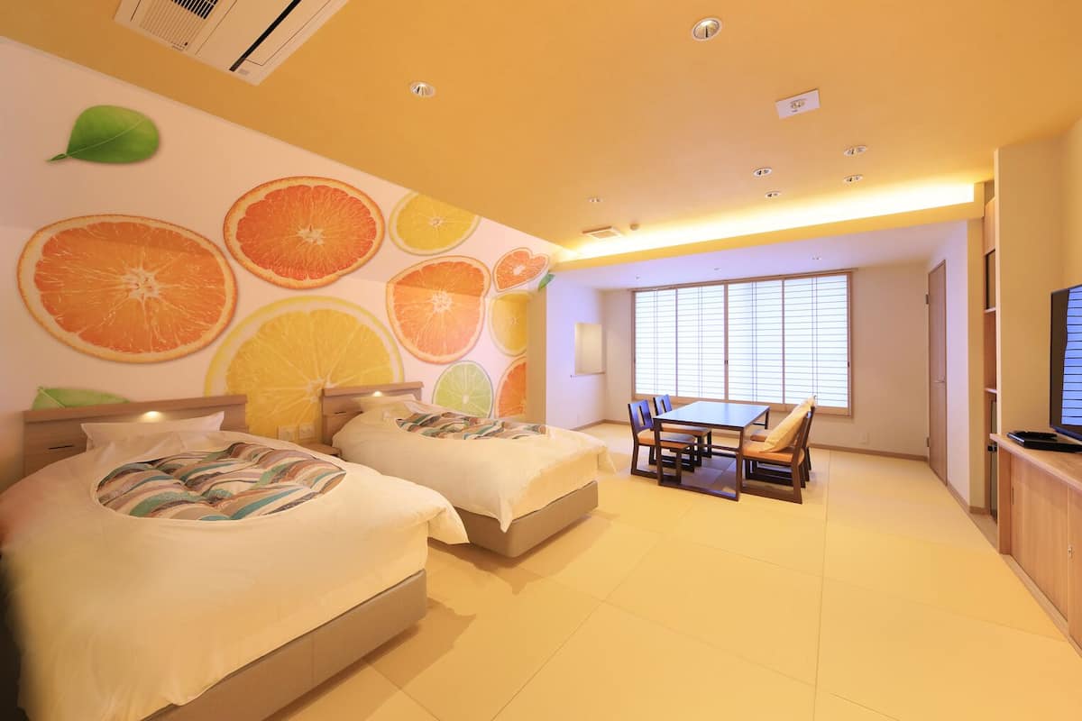 A hotel room with two beds, a dining table, and a large window with blinds.