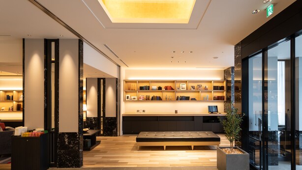 A modern lobby with a seating area, a reception desk, and a display of books and decor items. - JR WEST GROUP VIA INN Iidabashi Korakuen (Tokyo)