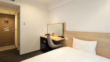 Een hotelkamer met een bed, een bureau met stoel, een spiegel en een houten deur.