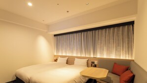 A hotel room with a large bed, a small sofa, a wooden side table, and a window with curtains. - JR WEST GROUP VIA INN Iidabashi Korakuen (Tokyo)