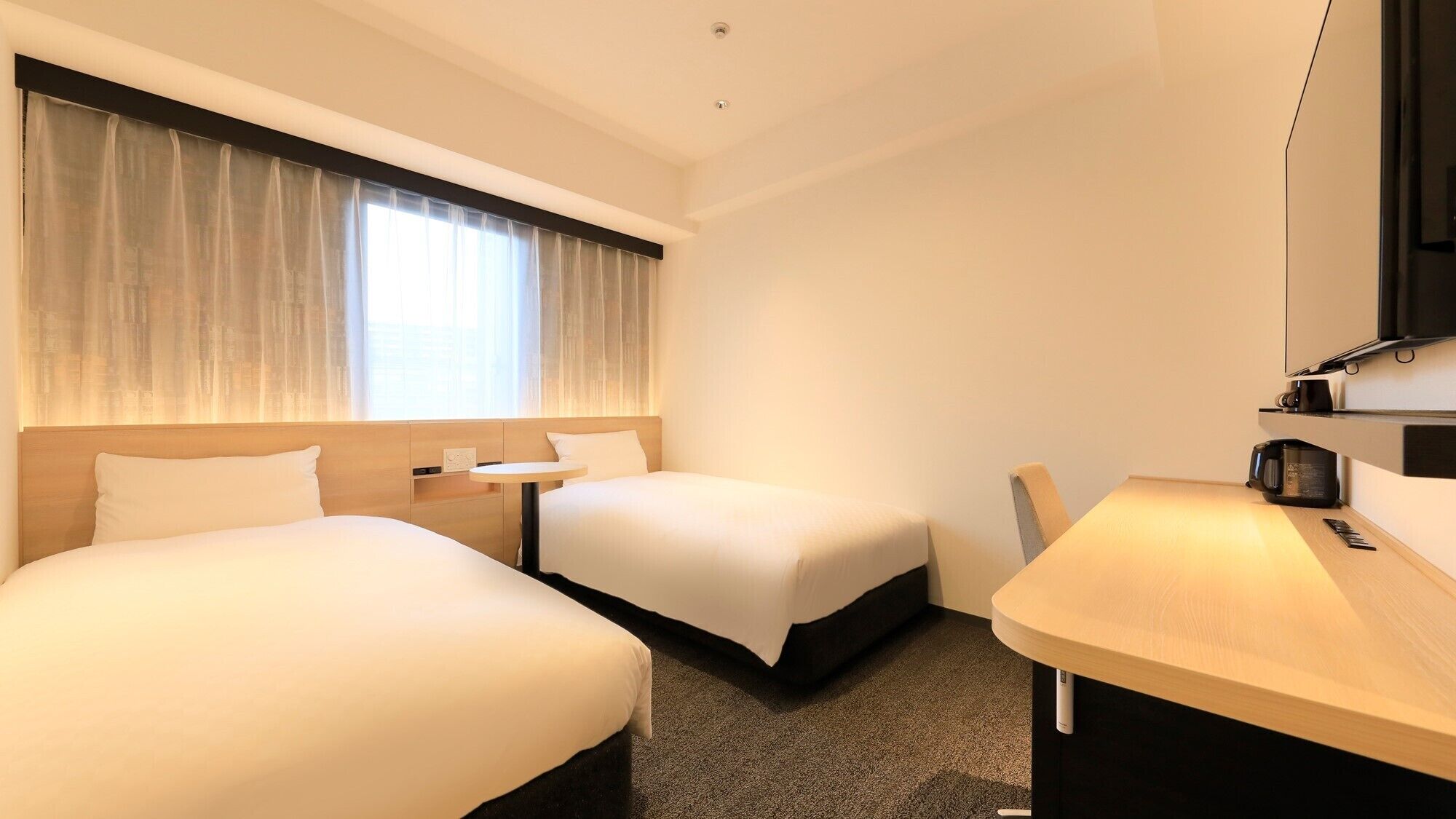 Habitación de hotel con dos camas, un escritorio, una silla, un televisor y una ventana con cortinas.