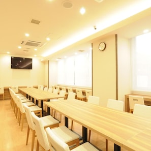 A conference room with long tables and chairs, a clock on the wall, and a large window.