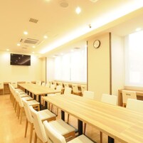 Un salón de conferencias con largas mesas y sillas, un reloj en la pared y un amplio ventanal.