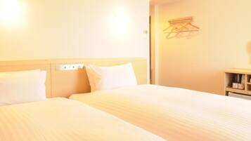 A hotel room with two beds, an air conditioning unit, a bedside table with a cup, and a wall-mounted drying rack.