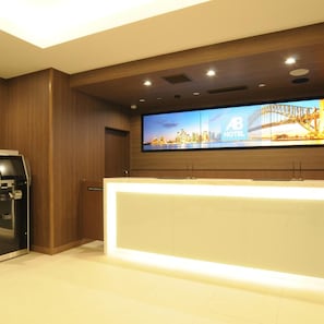 A hotel reception area with a large flat-screen TV displaying a cityscape, a reception desk, and a minibar.