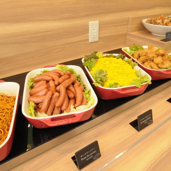 A buffet with various dishes including sausages, scrambled eggs, and a salad.