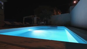 A nighttime swimming pool with clear water, surrounded by lounge chairs and a covered area. - B&B Rita and Family (Loceri)