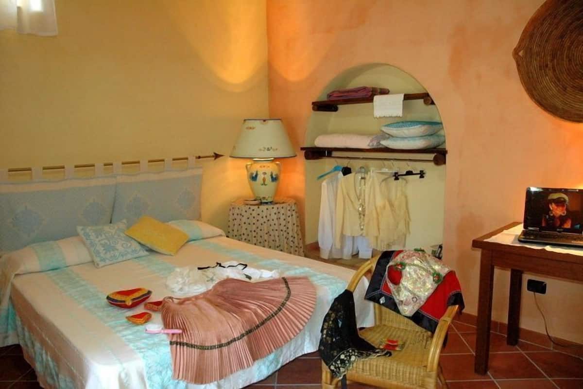 A bedroom with a bed, a lamp, a chair, a shelf with clothes, and a television.
