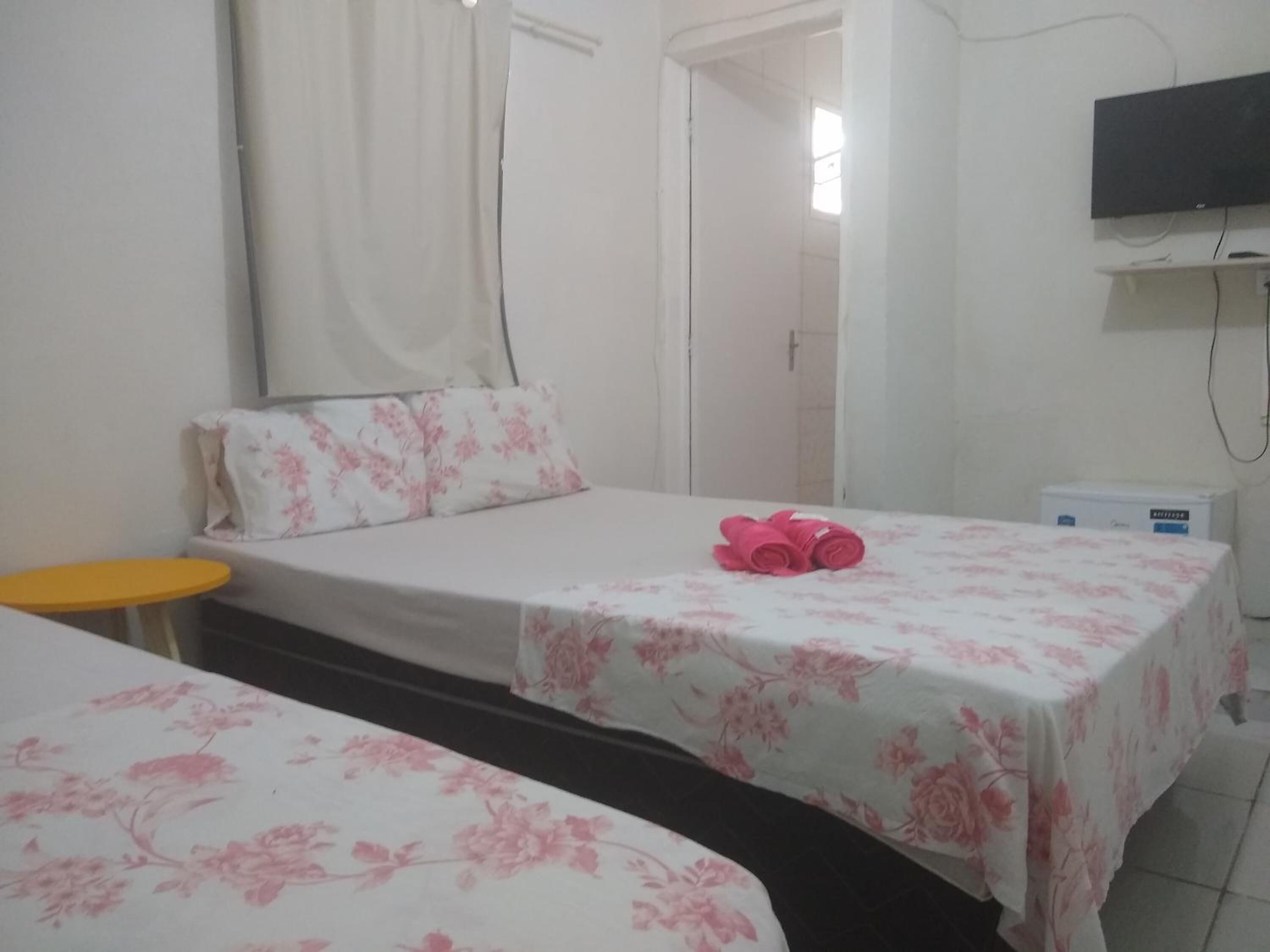 Una habitación con dos camas, cada una con colcha estampada y una mesita amarilla, además de un televisor montado en la pared.