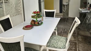 A dining area with a white table, four chairs, and a fruit display. - Casa da Esquina Pousada (Recife)