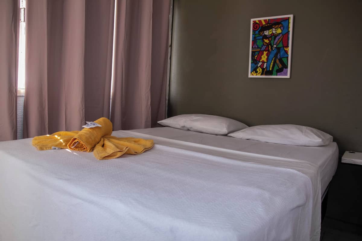 A hotel room with a bed, curtains, and a colorful painting on the wall.