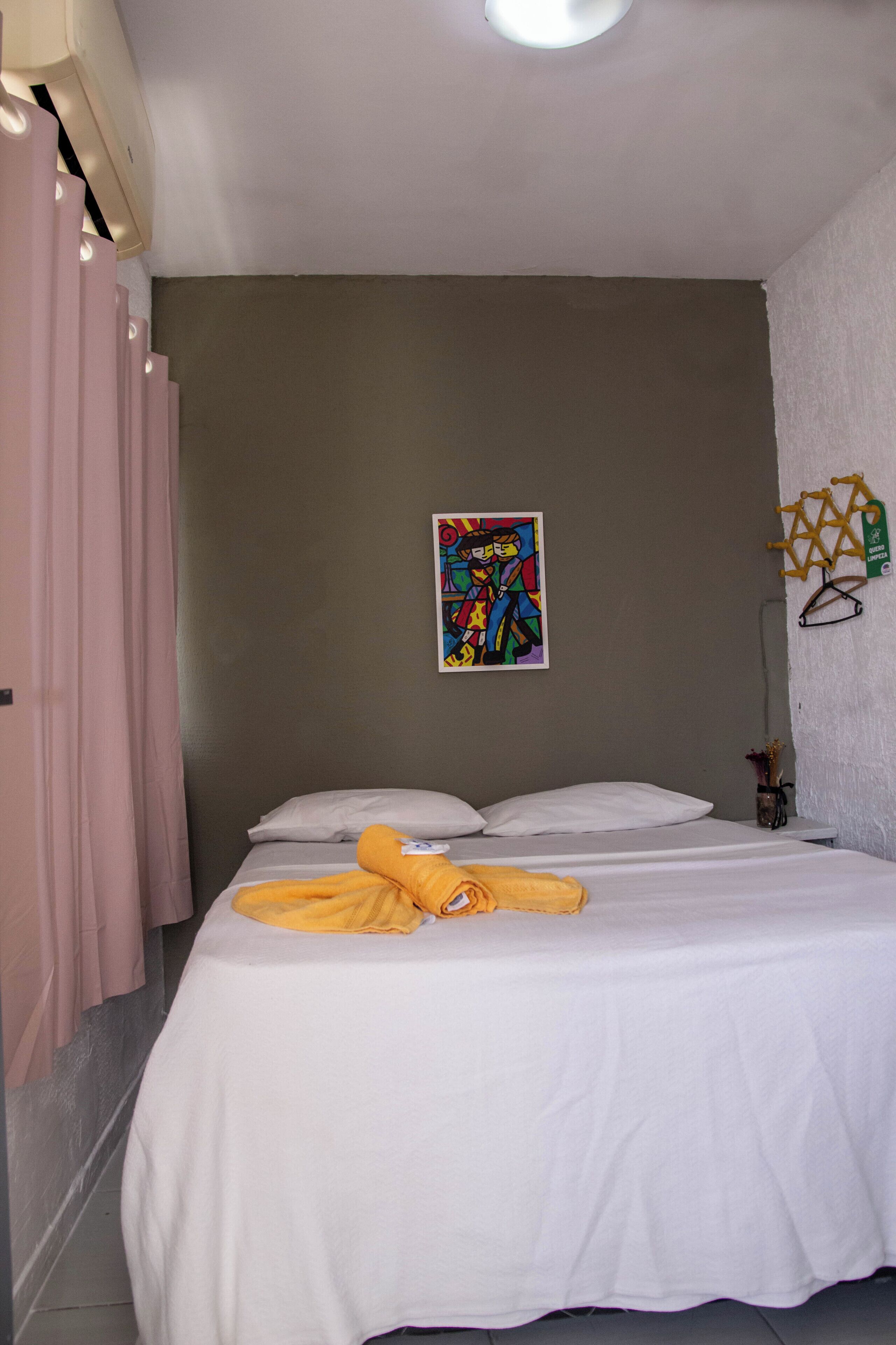 Un dormitorio con cama, ropa de cama blanca, un cuadro colorido en la pared y una ventana con cortinas.