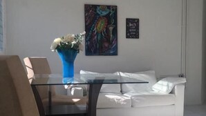 A modern living room with a glass dining table, beige chairs, a white sofa, and a blue vase with flowers. - Casa da Esquina Pousada (Recife)