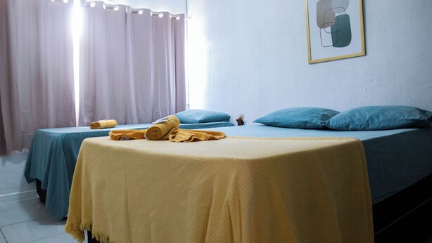 A room with two beds, each with a blue bedspread and pillows, and a yellow blanket on the bed in the foreground. - Casa da Esquina Pousada (Recife)