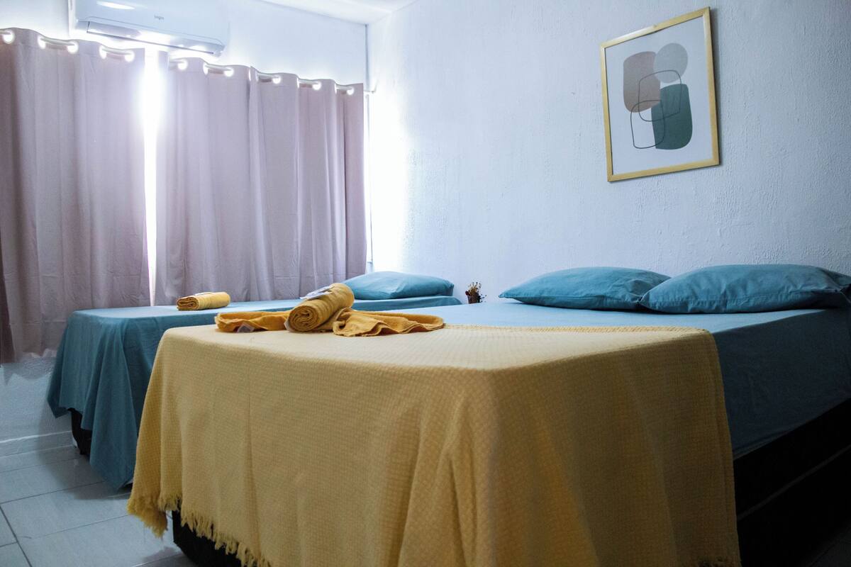 A room with two beds, each with a blue bedspread and pillows, and a yellow blanket on the bed in the foreground.