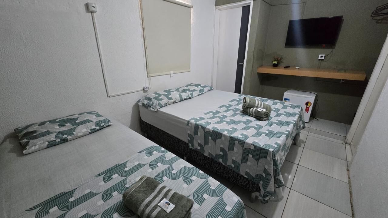 A small, compact room with two beds, a television, and a small refrigerator.