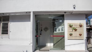 A building entrance with a glass door, a small step leading up, and a wooden panel with potted plants on the right. - Casa da Esquina Pousada (Recife)