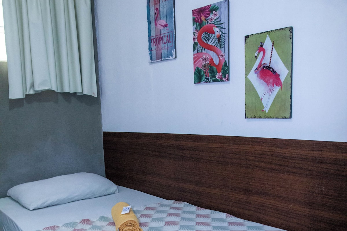 A neatly made bed with a patterned bedspread, a pillow, and a rolled towel on the bed. There are three wall art pieces above the bed.