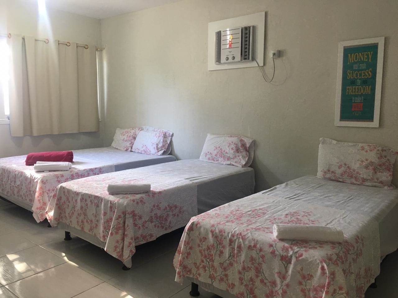 Habitación con tres camas individuales, cada una con colcha y almohadas estampadas con motivos florales, un calentador de pared y un cartel motivacional.