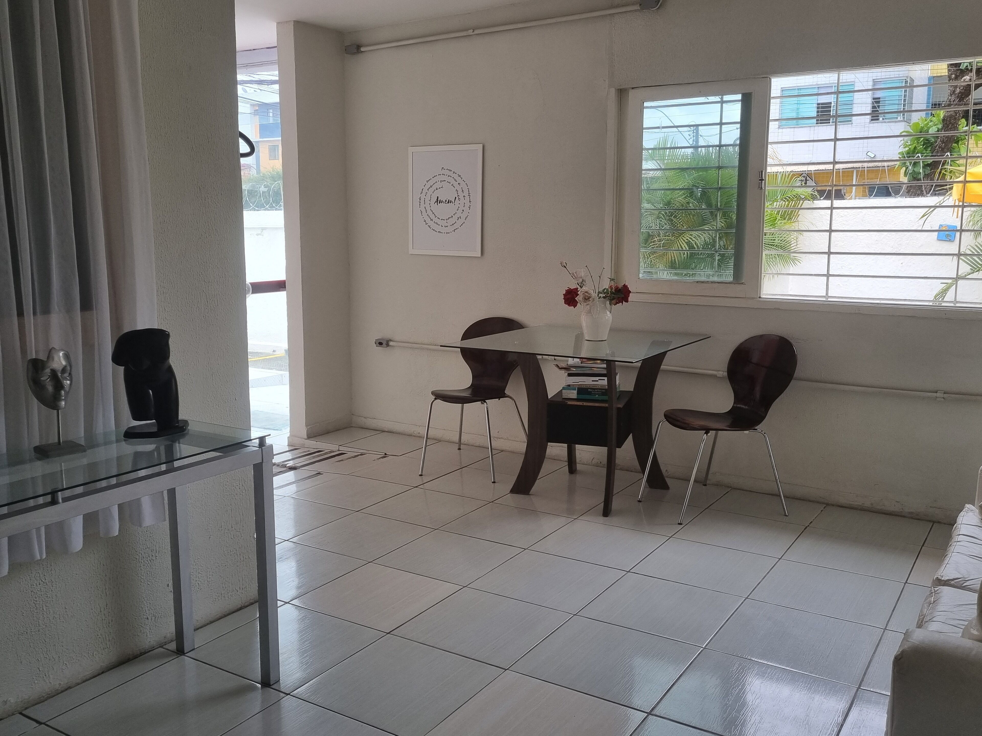 A modern room with a glass table, two chairs, a vase with flowers, and a framed artwork on the wall.