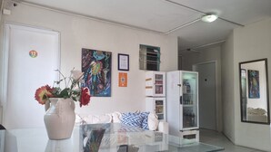 A hotel room with a glass table, a white sofa, a cabinet with glass doors, a painting on the wall, and a vase with flowers. - Casa da Esquina Pousada (Recife)