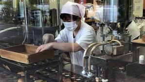 A person in a white uniform and pink head covering working at a food preparation station with multiple cooking pans and a wooden tray. - Phoenix Hotel (Tsu)