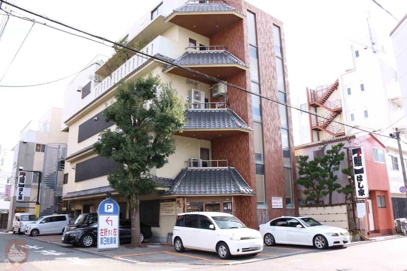 A multi-story building with a traditional tiled roof, a parking sign indicating a parking area, and several parked cars.