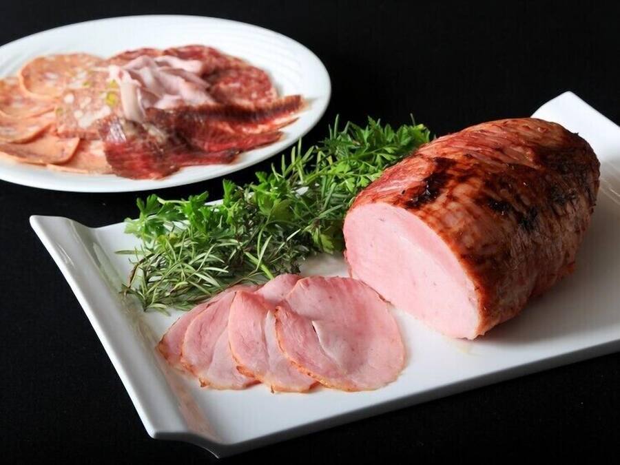 Une assiette avec des tranches de jambon et un jambon entier, sur l’os.