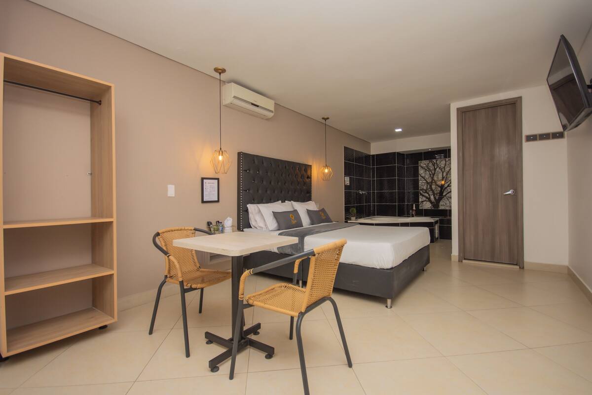 Quarto moderno com cama, mesa de cabeceira e cadeiras.